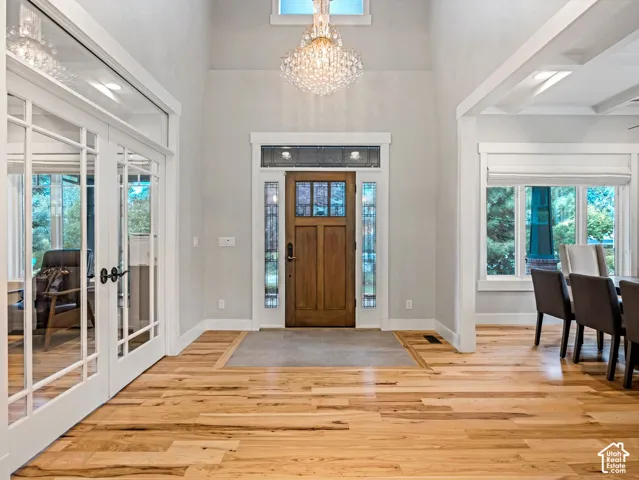 Entryway featuring high ceilings, wood-finish flooring, a crystal chandelier, and a wood-paneled door with decorative glass sidelights and transom