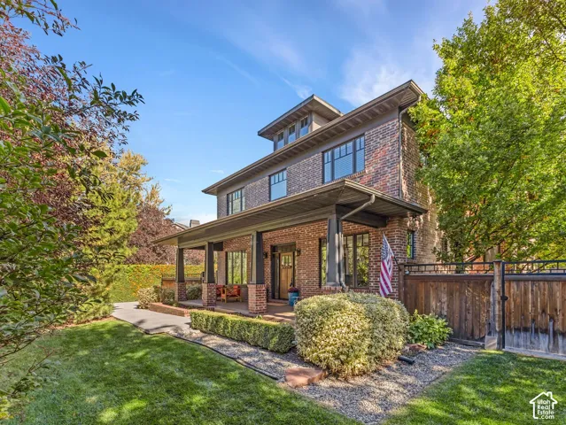Multi-story brick exterior featuring a covered front porch with square columns, dormer window, and mature landscaping