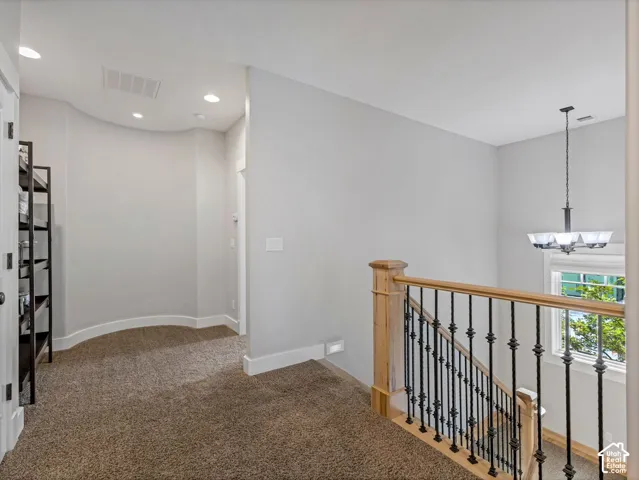 Curved wall detail featuring neutral wall tones, recessed lighting, and a staircase with natural wood handrails and black iron balusters, complemented by a multi-arm chandelier