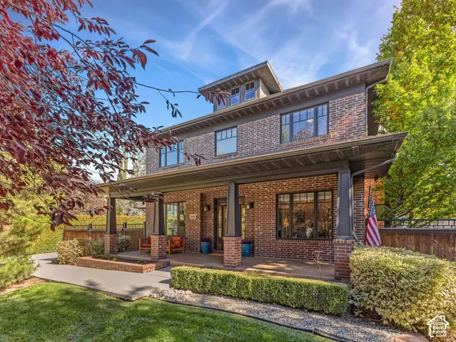 Three-story brick exterior featuring a covered front porch, dark-trimmed multi-pane windows, square support columns, and a dormer roofline