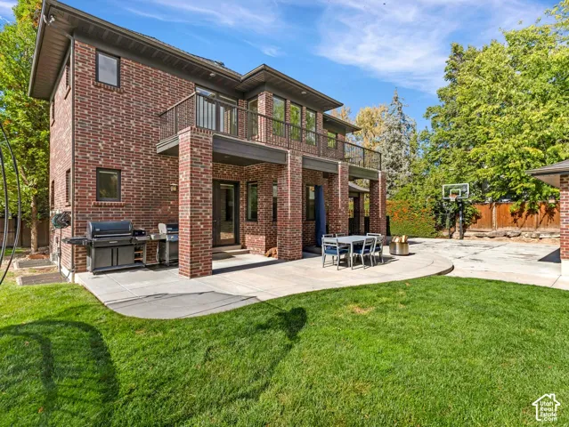 Multi-story brick exterior featuring a second-level balcony with metal railing, a concrete patio, and a backyard with mature trees