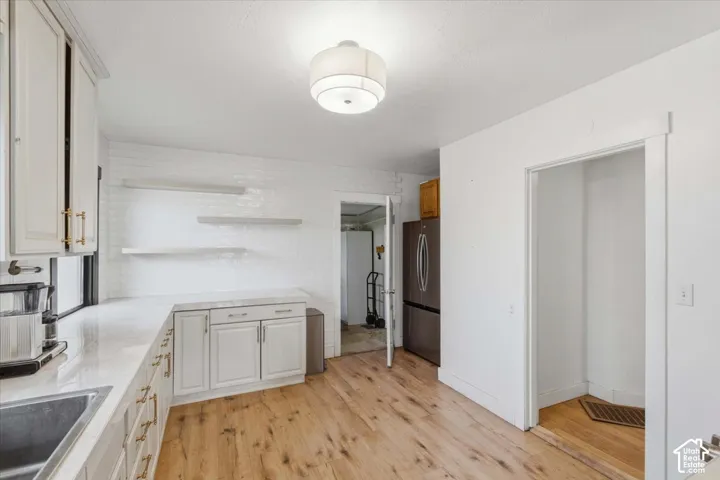 Kitchen featuring white cabinetry with gold-toned hardware, quartz countertops, white tile backsplash, floating shelving, and wood-finish flooring