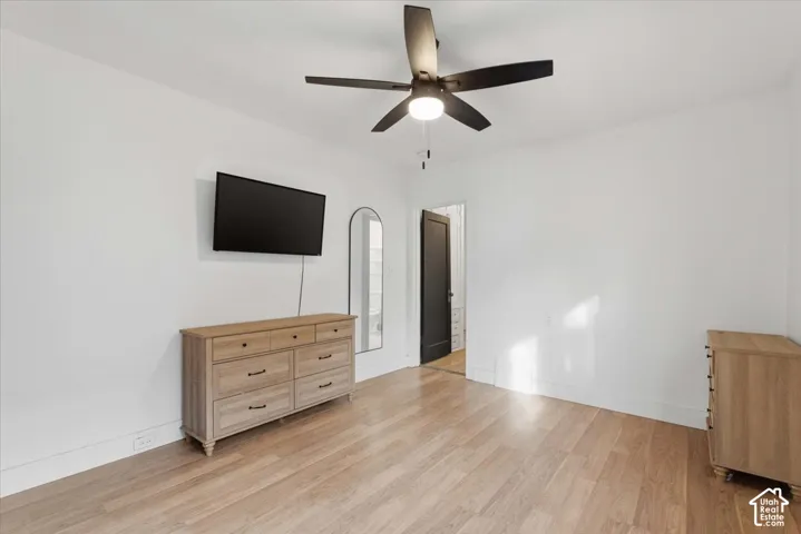 Neutral interior space featuring wood-finish flooring, a matte black multi-blade ceiling fan with integrated lighting, and a solid-core black interior door