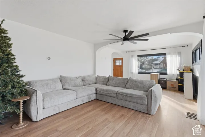Living area featuring wood-finish flooring, arched doorways, a multi-blade ceiling fan, and a wood-frame exterior door with glass detailing
