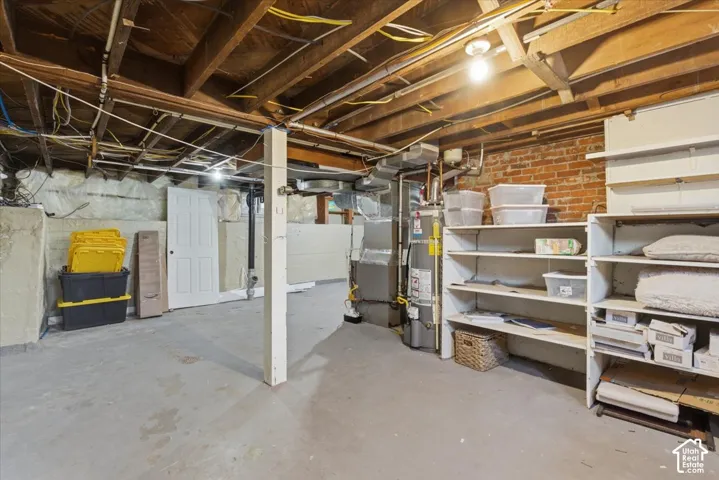 Unfinished basement featuring exposed wood ceiling joists, exposed brick walls, concrete flooring, and built-in shelving