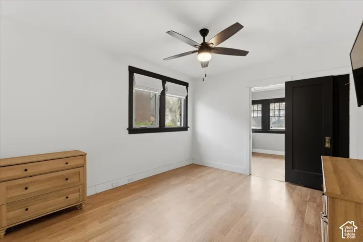 Interior room featuring light wood-finish flooring, high-contrast black window casings, a five-blade ceiling fan with integrated lighting, and a solid black interior door