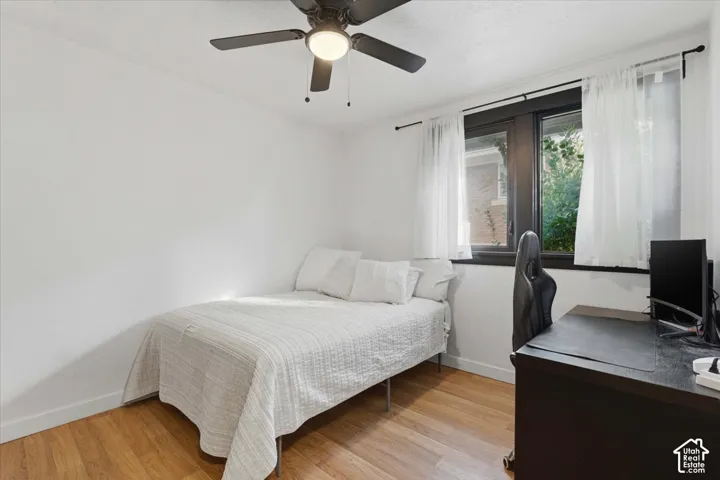 Room interior featuring wood-finish flooring, a ceiling-mounted light fixture with fan, and a window with dark-toned casing