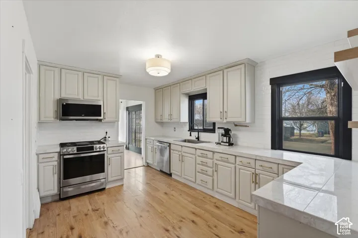 Kitchen featuring wood-finish flooring, shaker-style cabinetry, stainless steel appliances, white subway tile backsplash, and quartz countertops