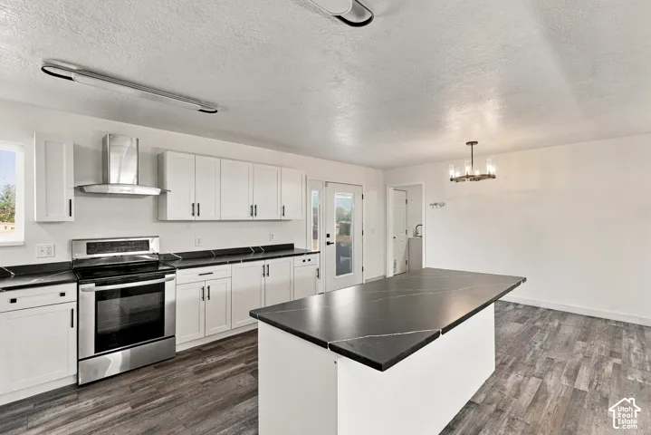 Kitchen featuring white shaker-style cabinetry, dark stone-finish countertops, a central island, stainless steel range with overhead vent hood, and wood-finish flooring