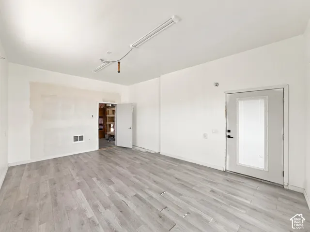 Interior room featuring wood-finish flooring, white walls, a flush-mount overhead light fixture, and an exterior door with a glass insert