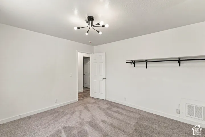 Neutral wall palette, multi-arm sputnik-style ceiling fixture, wall-mounted shelving unit with integrated hanging rod, and textured carpeting
