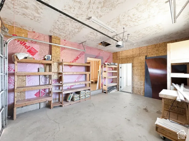Garage interior featuring exposed wood-stud walls, concrete flooring, integrated ceiling-mounted light fixtures, and multi-level built-in wooden shelving units
