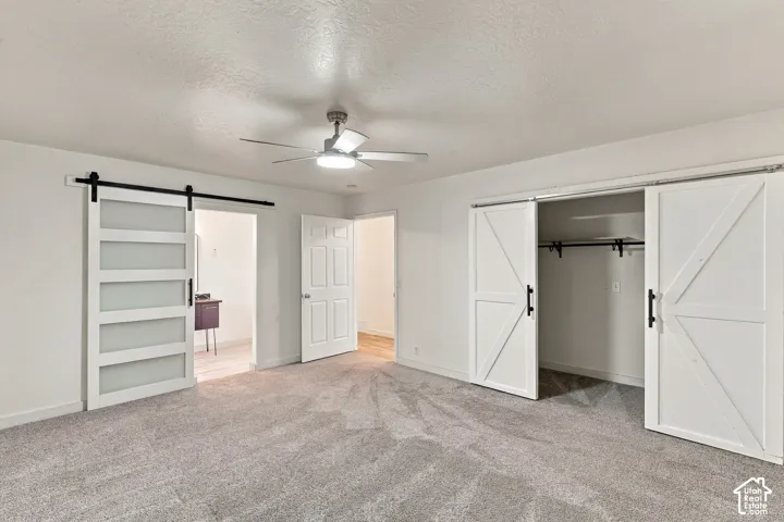 Interior space featuring neutral carpeting, a central ceiling fan with integrated lighting, a frosted glass paneled barn door, and dual white farmhouse-style sliding barn doors opening to a closet