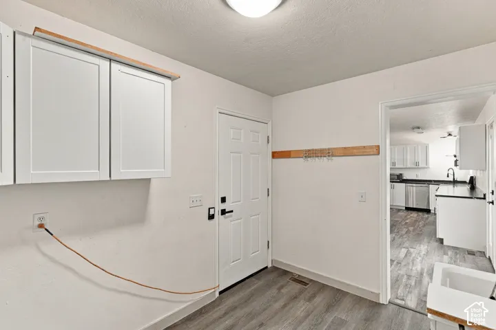 Utility area featuring white shaker-style wall-mounted cabinetry, wood-finish flooring, a mounted wood coat rack, and a dedicated utility sink