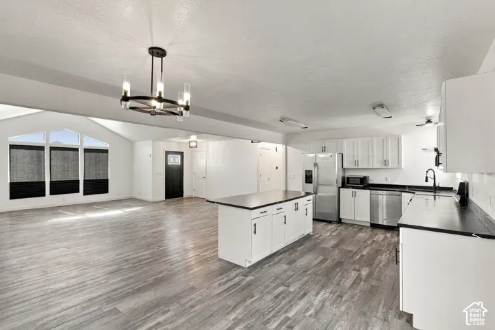 Kitchen featuring white shaker-style cabinetry, dark solid-surface countertops, stainless steel appliances, a center island, and wood-finish flooring