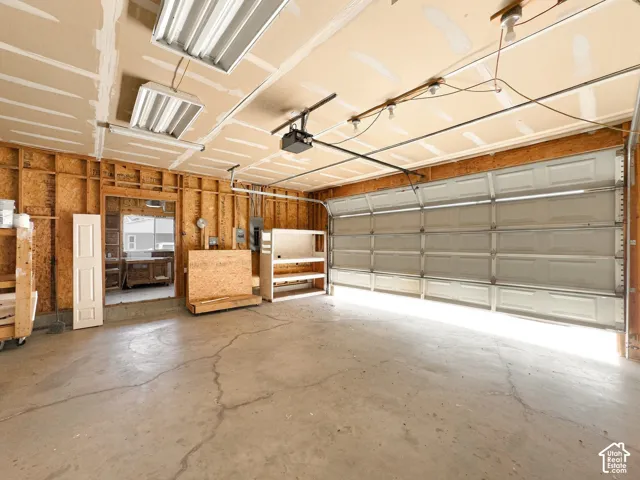 Multi-car garage featuring a concrete floor, sectional overhead door, ceiling-mounted fluorescent lighting, and exposed timber stud framing