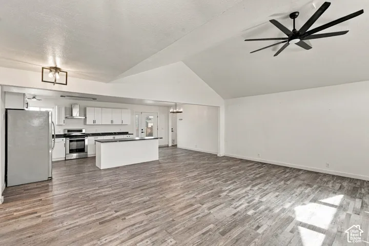 Vaulted ceiling featuring a multi-blade ceiling fan, wood-finish flooring, white cabinetry, dark countertops, and stainless steel kitchen appliances