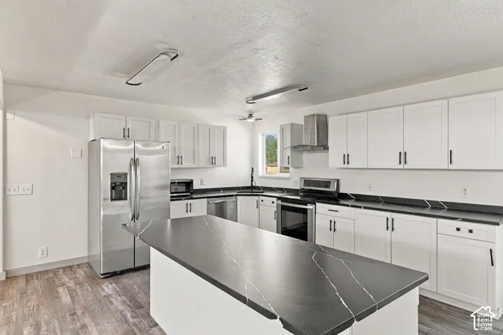 Kitchen featuring white shaker-style cabinetry, dark stone countertops with light veining, a central island, stainless steel appliances, and wood-finish flooring