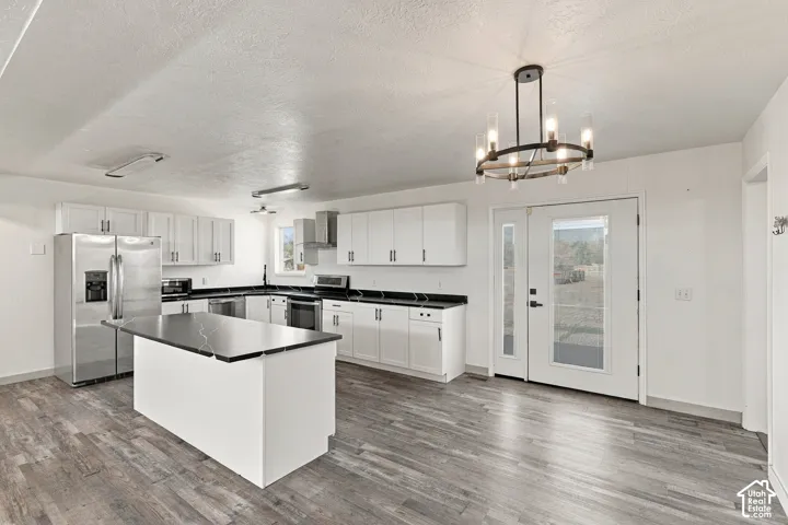 Kitchen featuring white cabinetry, dark countertops, an island, stainless steel appliances, and a circular chandelier