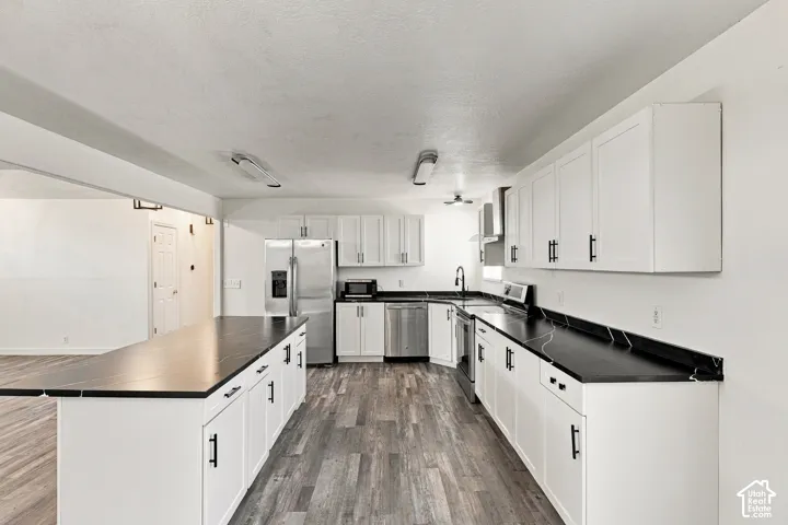 Kitchen featuring white shaker-style cabinetry, dark stone-finish countertops, stainless steel appliances, and wood-finish flooring