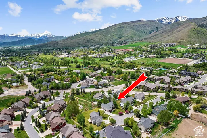 Aerial perspective featuring a residential property situated in a mountainous landscape with snow-capped peaks, expansive greenery, mature trees, and a cul-de-sac configuration