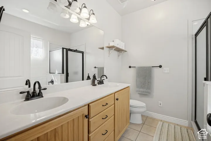 Bathroom featuring a double-sink vanity with wood-finish cabinetry, solid-surface countertops, oil-rubbed bronze fixtures, a large wall-mounted mirror, and a walk-in shower with a glass enclosure