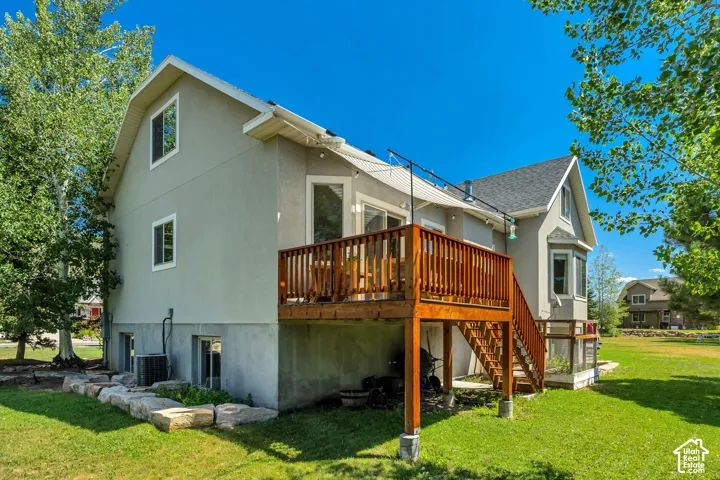 Stucco exterior home featuring a raised wooden deck, staircase, concrete foundation, and stone landscaping border