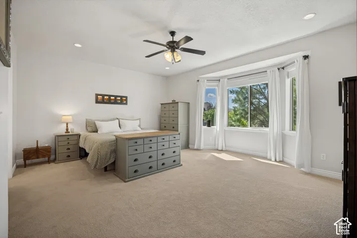 Neutral-toned carpeting, recessed ceiling lighting, bay window, and a central ceiling fan with integrated lighting