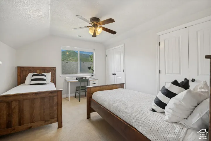 Vaulted ceiling, ceiling fan with light fixture, dual-door closet, and window with mountain scenery
