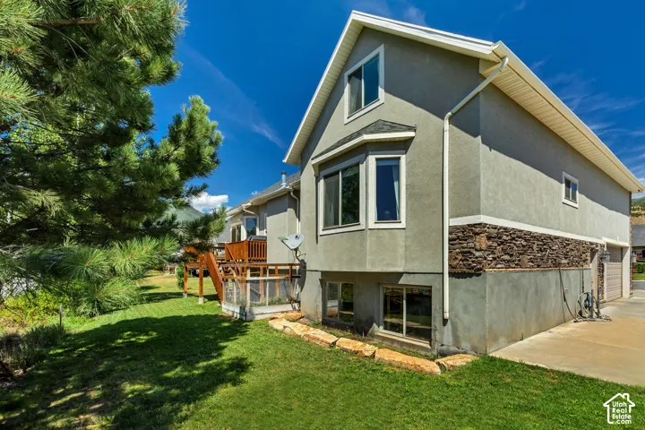 Multi-level exterior featuring stucco siding, stone veneer accents, a wood deck with railings, and large bay windows