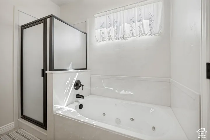 Jetted soaking tub with tile surround, enclosed walk-in shower with frosted glass panels, and dark-finish hardware