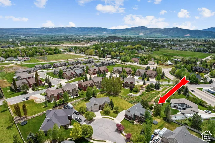 Aerial perspective of a multi-level residential property featuring a multi-car garage, pitched roofline, and established landscaping set against a mountain backdrop