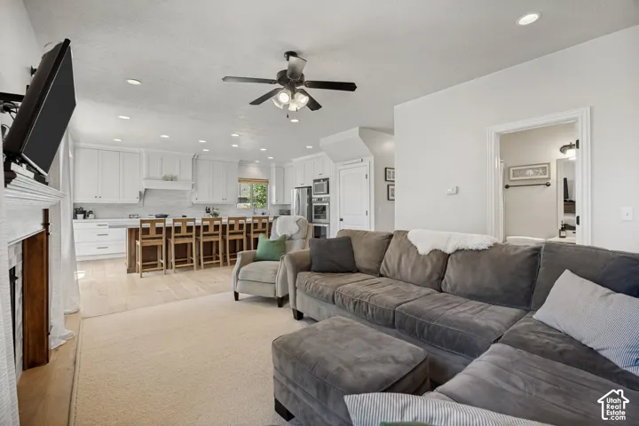 Open-concept area featuring white cabinetry, wood-finish flooring, a stone-surround fireplace, recessed lighting, and a built-in oven