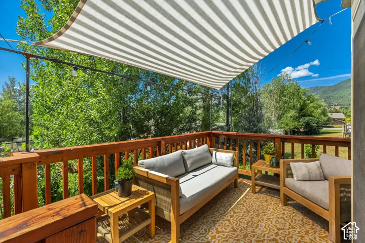 Elevated wooden deck featuring a stained wood railing, overhead sun shade canopy, and mountain scenery