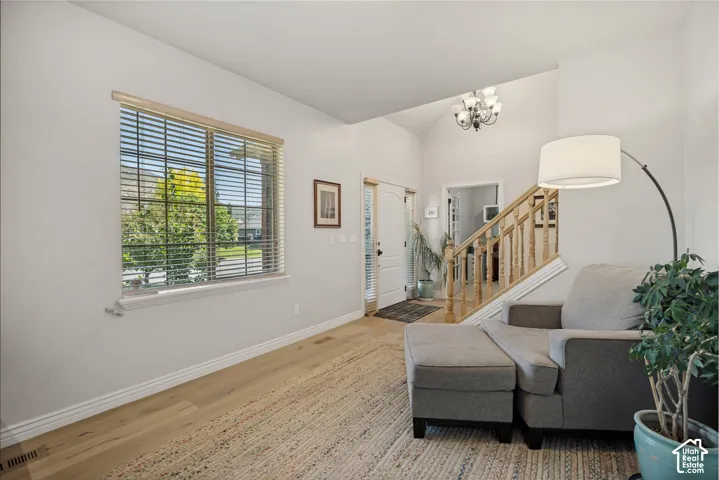 Entryway featuring vaulted ceilings, light-toned wood-finish flooring, a multi-tiered chandelier, and a wood banister railing
