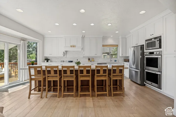 Kitchen featuring white shaker-style cabinetry, a central island with countertop seating, stainless steel appliances, recessed ceiling lighting, and wood-finish flooring