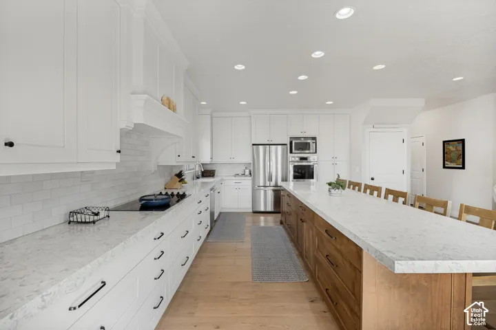 Kitchen featuring custom white cabinetry, stone countertops, a large wood-finish center island, stainless steel built-in appliances, and wood-finish flooring