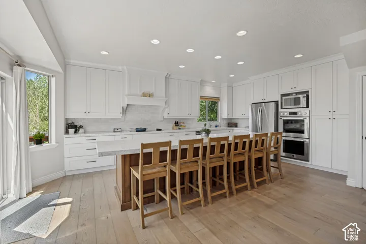Kitchen featuring white cabinetry, an expansive central island with stone-surface countertop, recessed lighting, stainless steel wall-mounted oven and microwave, and wood-finish flooring