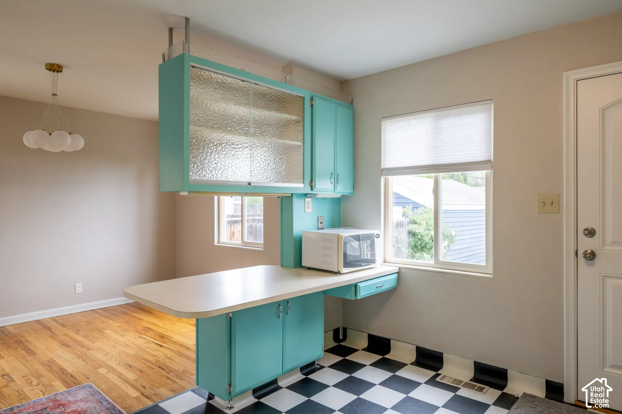 Mid-century style kitchen featuring custom teal cabinetry, textured glass cabinet fronts, integrated countertop peninsula, and a checkerboard pattern floor
