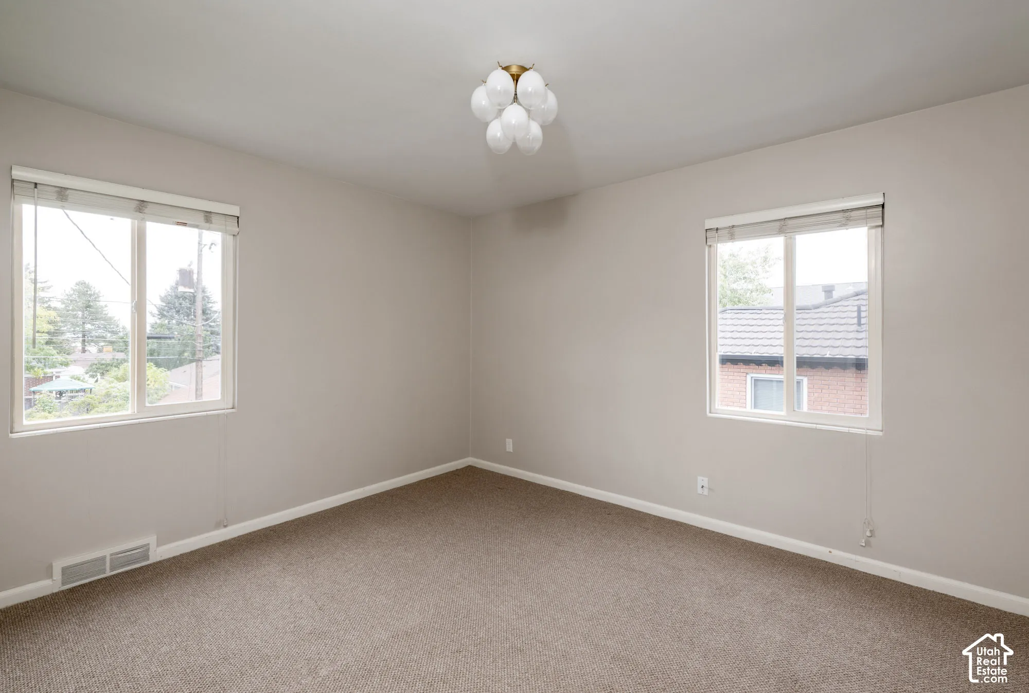 Neutral interior featuring wall-to-wall carpeting, two dual-pane windows with integrated blinds, and a multi-globe flush-mount light fixture with a metallic finish