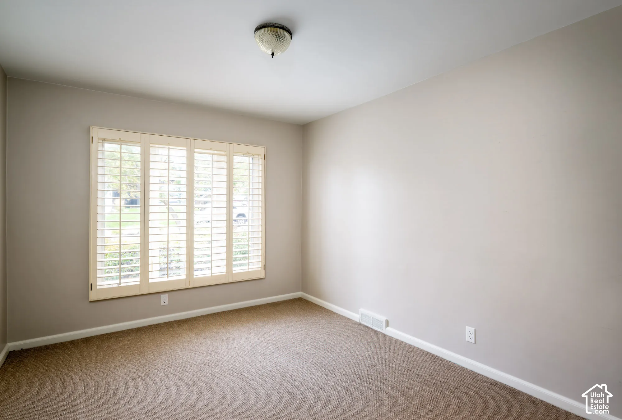 Neutral-toned interior space featuring neutral wall paint, wall-to-wall carpeting, and a multi-panel window with built-in plantation shutters