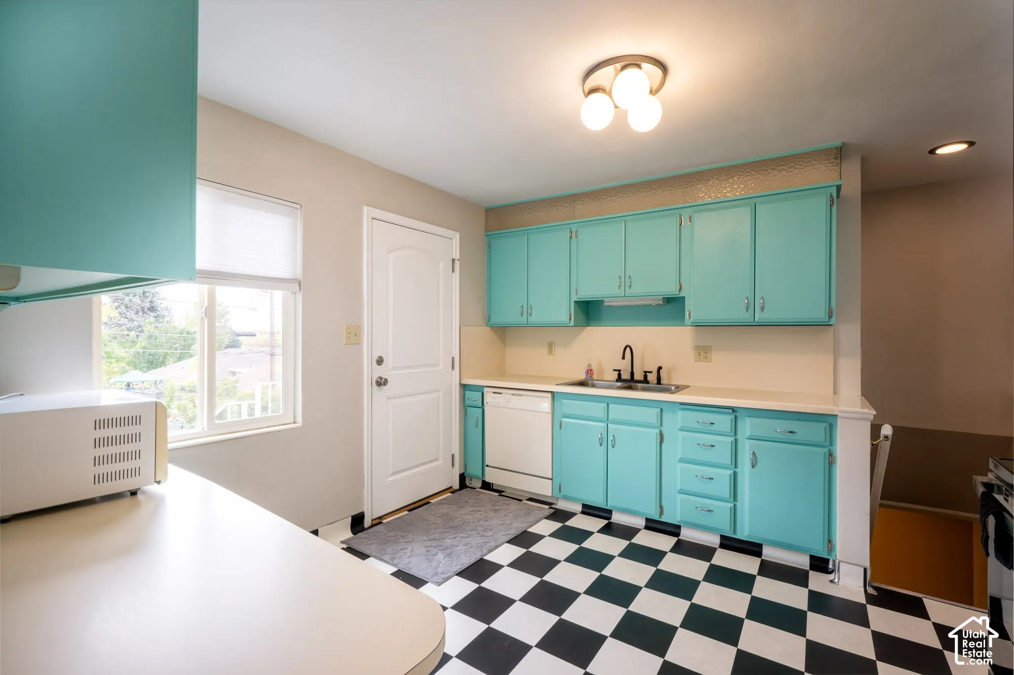 Kitchen featuring custom cabinetry, checkerboard tile flooring, dual-basin sink with a matte black faucet, and built-in dishwasher