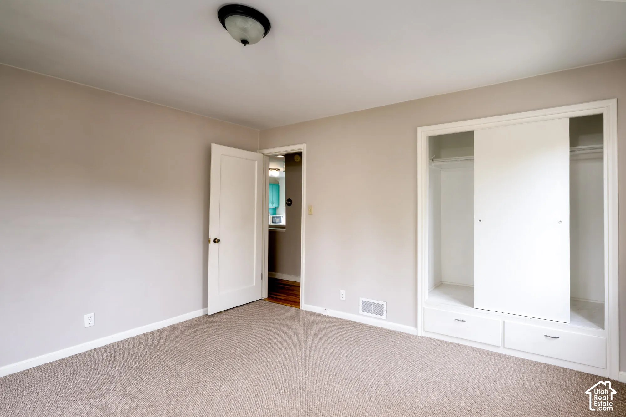 Room with neutral carpeting and a built-in closet system featuring sliding doors and lower drawers