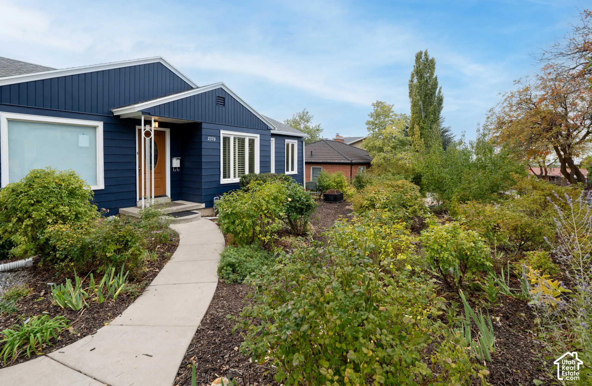 Blue horizontal siding exterior featuring a concrete walkway, mulched garden beds, and mature landscaping