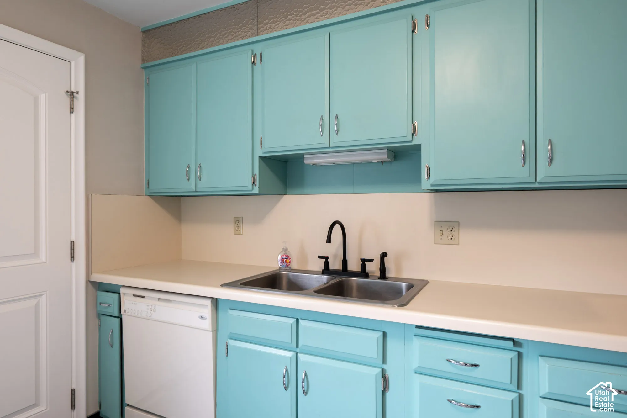 Kitchen featuring solid-color cabinetry, dual-basin stainless steel sink, matte black gooseneck faucet, integrated dishwasher, and solid-surface countertop
