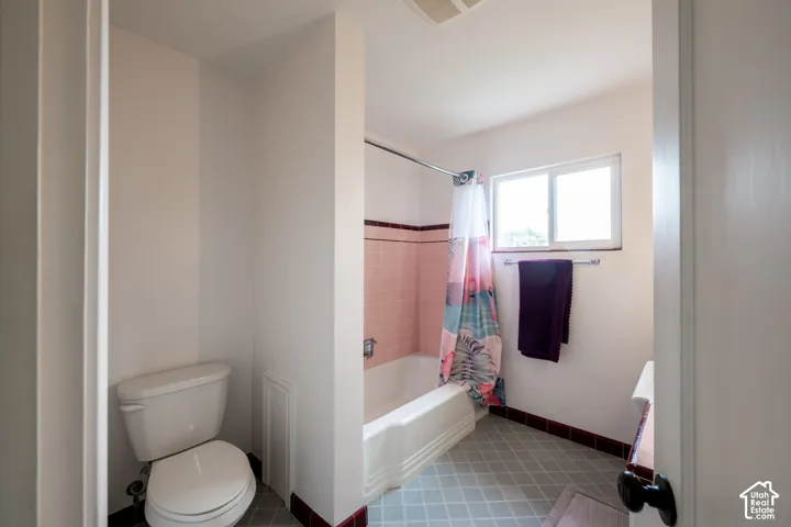 Bathroom featuring a porcelain tub, ceramic wall tiling, a sliding window, and a white toilet