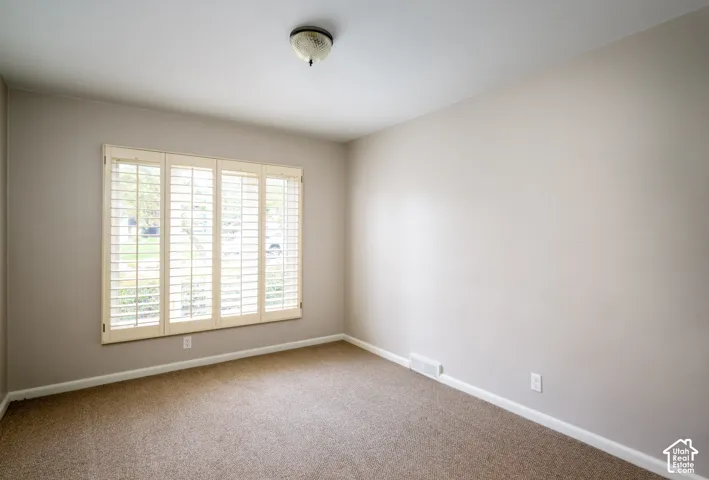 Neutral-toned interior space featuring neutral wall paint, wall-to-wall carpeting, and a multi-panel window with built-in plantation shutters