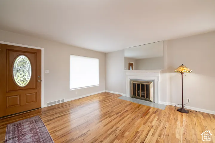 Hardwood flooring, wood entry door with oval decorative glass insert, fireplace with white mantle, stone hearth, and oversized wall-mounted mirror