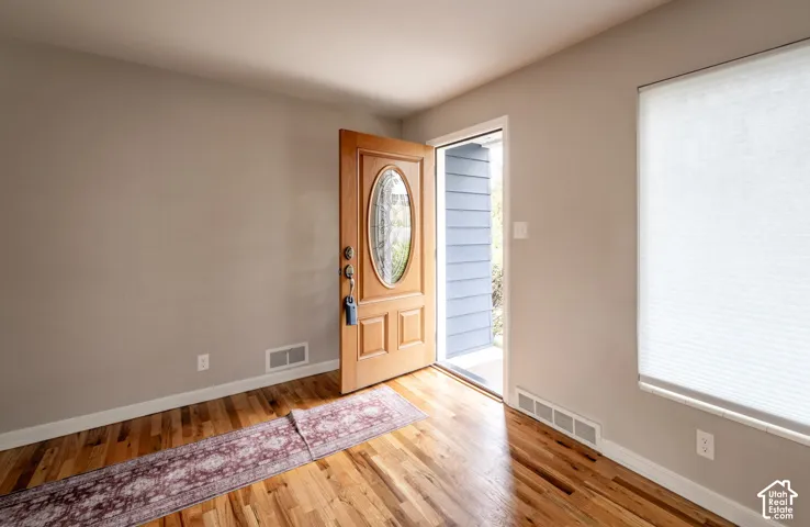 Entry featuring wood-finish flooring, a solid wood door with a decorative oval glass insert, and a wall-mounted cellular shade
