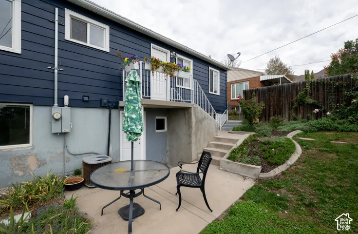 Exterior elevation featuring horizontal lap siding, a concrete patio, integrated staircase with metal railing, and tiered garden beds